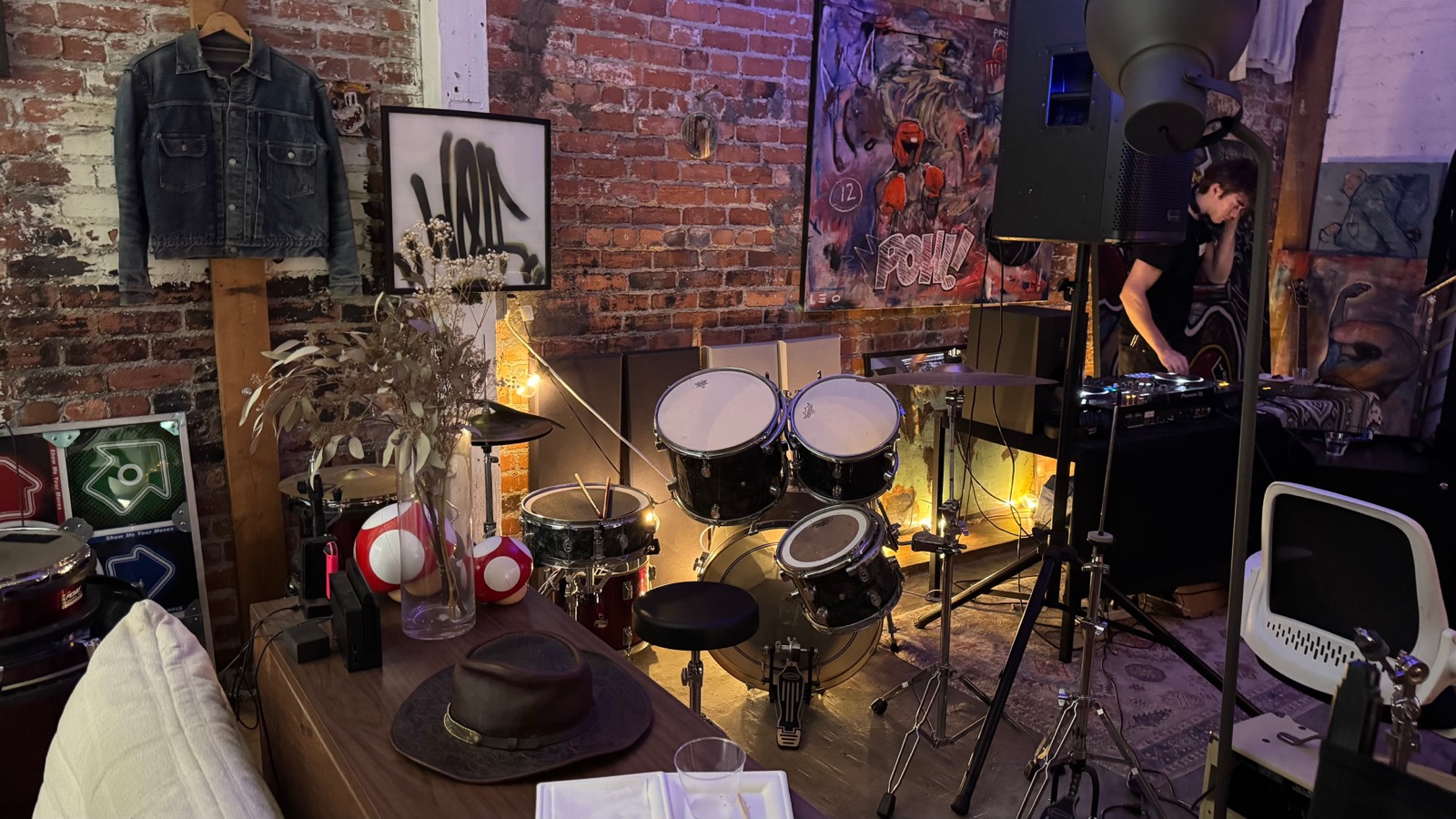 A room with a drum kit up front and DJ decks in the corner